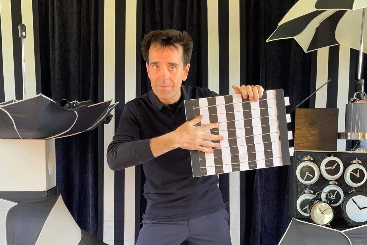 Monsieur Fred sur scène, réalisant un numéro de magie et d’illusion d’optique devant un décor en noir et blanc